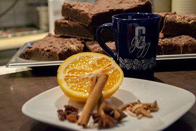 Bild mit einer Tasse schwedischen Glühwein, im Hintergrund Schokoladenkuchen. Im Vordergrund ein Teller mit typischen Zutaten für den schwedischen Glühwein.